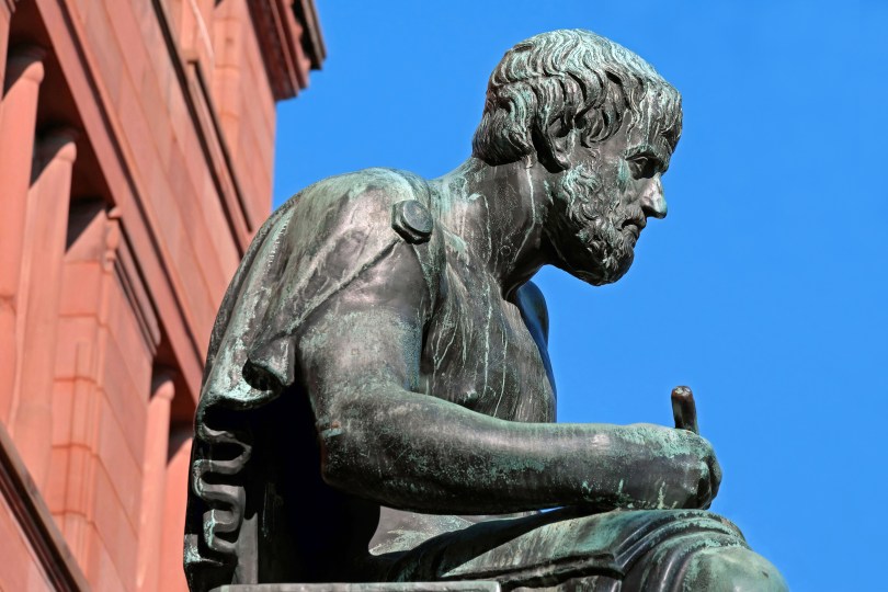 A bronze statue of Aristotle with a pen engaged in the flow of thought